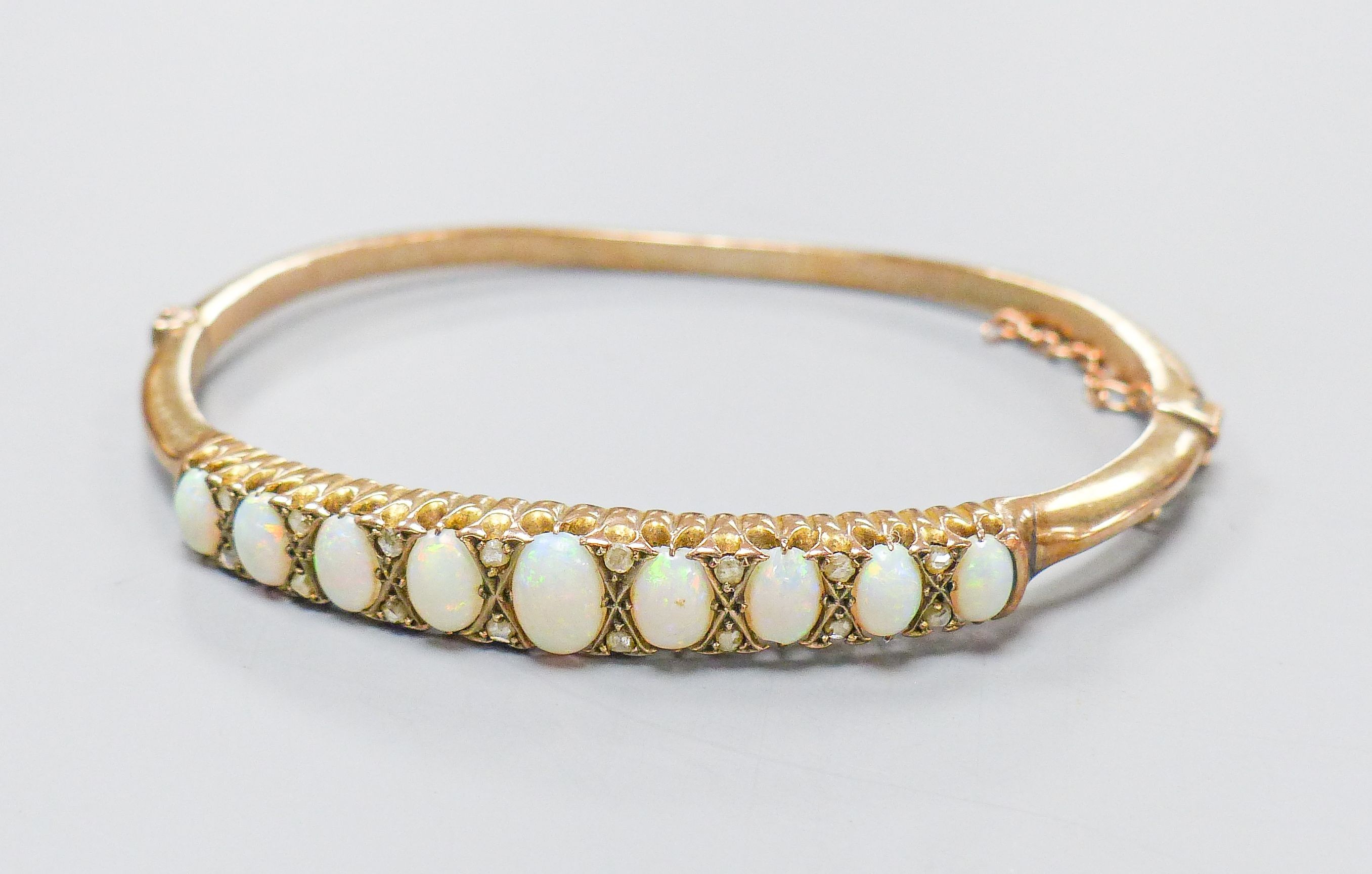 An early 20th century gold plated graduated nine stone white opal set hinged bracelet, with diamond chip spacers, in fitted box.